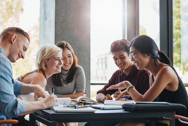 Blog - College Students Sitting at a Table Talking and Laughing Next to a Large Window with Sunshine Pouring Through